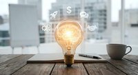 Glowing light bulb on wooden desk with business icons floating above in modern office environment representing innovation and creative ideas.