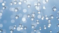 Transparent glossy bubbles floating on a soft blue bokeh background, evoking freshness, hydration, and purity for cosmetic or wellness design.