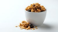 Homemade granola with nuts and dried fruits in white bowl on clean background for healthy breakfast and snacking concepts.