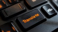 Black computer keyboard with illuminated orange translate button in dark environment, macro photography showing technology detail for language services.