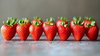 Fresh ripe strawberries arranged in row on rustic surface, showing gradient size from large to small. Vibrant red fruit with green stems and natural lighting.