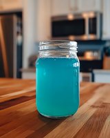Vibrant blue cocktail or refreshing summer drink served in classic mason jar on wooden table surface with modern kitchen background.