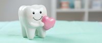 Cute cartoon tooth character holding pink heart on mint background for dental care and oral health education campaigns.