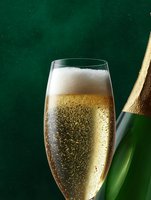 Glass of sparkling champagne with bubbles and foam against dark green background with bottle, close-up view for luxury celebration and wine design.