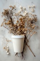 Dried wildflowers and delicate white blossoms arranged with takeaway coffee cup on textured light background, creating rustic botanical flat lay.