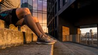 Young woman sitting on concrete ledge during golden hour sunset in urban city environment with modern buildings and warm lighting atmosphere.