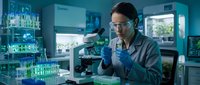 Female scientist examining samples through microscope in modern laboratory with test tubes and research equipment for medical analysis.