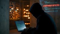 Hooded hacker in dark room working on laptop with glowing screen and digital code displays in cybersecurity attack scenario for technology concepts.