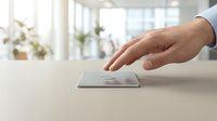 Male hand reaching toward modern smartphone on clean white desk in bright contemporary office workspace for business communication and technology.