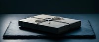 Elegant black gift box with silver ribbon on dark slate surface against moody background for luxury packaging and special occasions.