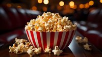 Fresh popcorn overflowing in classic red and white striped bowl against dark background with warm bokeh lights creating cozy cinema atmosphere.
