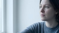 Thoughtful young Caucasian woman gazing out window in soft natural light, contemplating future possibilities in cozy indoor setting for wellness content.
