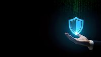 Businessman hand holding glowing blue shield icon on dark digital background with matrix code for cybersecurity and data protection concepts.