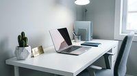 Minimalist home office workspace with open laptop on white desk, cactus plant, and modern chair in bright, clean interior.