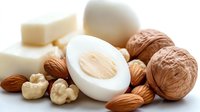 Protein-rich foods including hard-boiled eggs, assorted nuts, walnuts and cheese on white background. Healthy snack options for fitness nutrition.