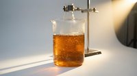 Amber liquid in glass beaker with metal stand and clamp, scientific laboratory setup for chemistry experiments, education, or research demonstrations.