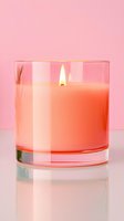 Glowing coral-colored scented candle in clear glass container on reflective surface against pink background, creating serene spa-like atmosphere.