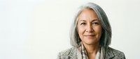 Confident mature Hispanic businesswoman with gray hair smiling in professional blazer against neutral background for corporate and leadership concepts.