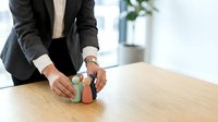 Professional businesswoman in dark suit holding colorful wooden house models on office desk, real estate investment concept for presentations.