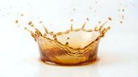 Golden liquid splash creating crown-shaped formation with droplets frozen in motion against clean white background for beverage advertising.