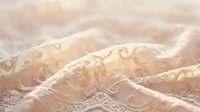 Delicate beige lace fabric with ornate floral embroidery and scrolling patterns, featuring soft folds and texture for fashion, textile, and design projects.