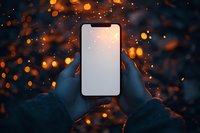 Hands holding smartphone with blank screen against magical bokeh lights background in evening atmosphere.