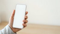 Hand holding smartphone with blank white screen against neutral background, suitable for app mockups, mobile technology presentations, and digital marketing campaigns.