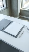 Minimalist workspace with blank notebook, pen and glasses on white desk near concrete wall and windows for business planning and creative writing.