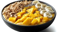 Healthy breakfast smoothie bowl topped with fresh mango slices, banana, granola and chia seeds in dark ceramic bowl on white background.