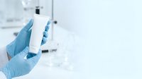 Scientist in blue latex gloves holding blank white product container in laboratory setting with equipment in background.