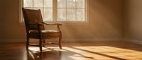 Wooden rocking chair in sunlit room with large window casting warm light on hardwood floor, creating peaceful interior ambiance.