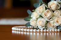 Elegant cream roses bouquet with pearl necklace on wooden surface, soft focus background creates romantic wedding atmosphere. Luxury floral arrangement for bridal design.