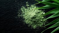 Green matcha tea powder scattered on dark stone surface with fresh bamboo leaves, creating dramatic contrast for culinary and wellness concepts.