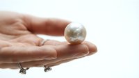 Hand holding a lustrous pearl sphere on white background, suitable for luxury jewelry, beauty, and premium product marketing.