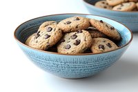 Fresh homemade chocolate chip cookies served in rustic blue ceramic bowl on white surface, showing soft, chewy texture with melted chocolate chunks.