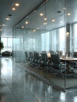 Modern glass-walled conference room with black leather chairs and city skyline view in contemporary corporate office building interior.