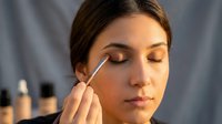 Young woman applying eyeshadow with makeup brush in soft natural light. Professional beauty routine and cosmetics application concept.