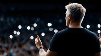 Mature businessman speaking at corporate conference with stage lights and audience in background for presentations and leadership events.