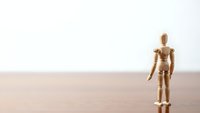 Wooden artist mannequin figure standing alone on wood surface against white background for creative design and artistic projects.
