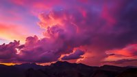 Dramatic purple and pink sunset clouds over mountain silhouettes creating vibrant evening sky with golden light rays for nature backgrounds and landscapes.