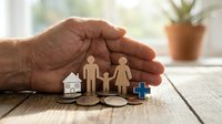 Protective hands covering wooden family figures with house and car symbols on rustic table representing life insurance and family security concept.
