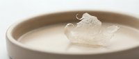Translucent ice cube floating in creamy white liquid within ceramic bowl, suitable for beverage, skincare, or cosmetic product photography and advertising.