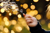 Magical moment with soap bubbles floating against golden bokeh lights at sunset, hand holding bubble wand creates dreamy atmosphere for childhood memories.
