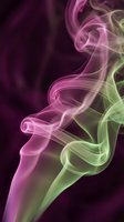 Colorful smoke swirls in pink and green hues creating elegant flowing patterns against dark background for creative design projects.