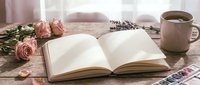 Open book with blank pages on rustic wooden table surrounded by pink roses, lavender sprigs and coffee mug creating cozy reading atmosphere for journaling.