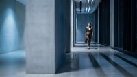 Professional businesswoman walking through modern corporate office corridor with dramatic lighting and contemporary architecture for business concepts.