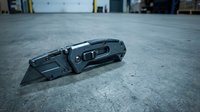 Black tactical folding knife with serrated blade on concrete warehouse floor for safety equipment and tool photography.