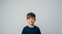 Young boy with light brown hair and fair complexion, wearing a dark navy t-shirt, smiling at camera against neutral gray background. Portrait suitable for family, education, healthcare and lifestyle marketing.