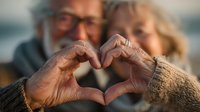 Elderly couple making heart shape with hands showing love and togetherness in golden light. Senior romance, relationship goals, Valentine's Day concept.
