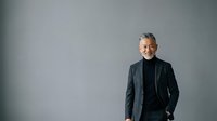 Mature man with gray hair and glasses wearing dark blazer and black turtleneck, standing confidently against neutral gray background, suitable for corporate, business, and professional portraits.